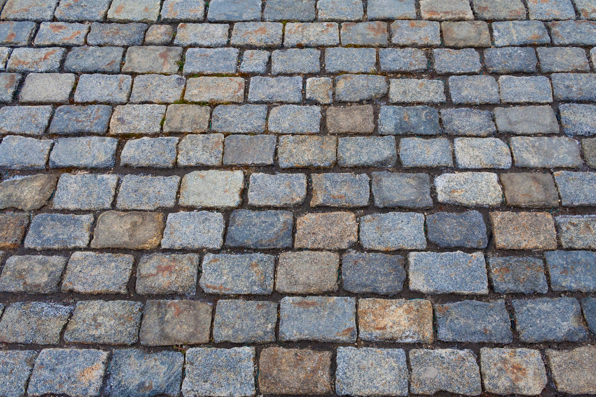 Weathered cobblestone street with gray and tan colored stones arranged in irregular rows.Retry